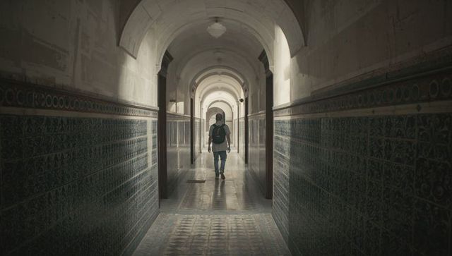 Backpack student walking down sunlit arched tiled corridor symmetry and perspective