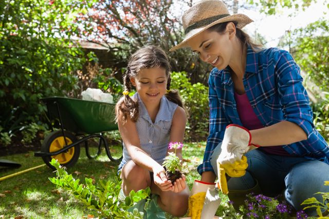 Smiling mother teaching daughter to plant seedlings while gardening in backyard 