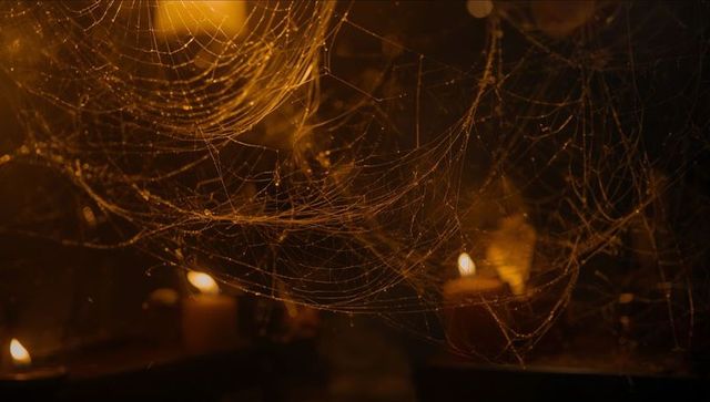 Intricate cobwebs glowing in candle-lit attic ambiance