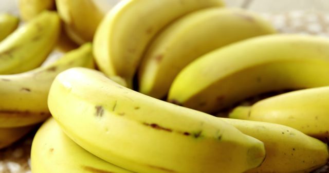 Image shows several yellow bananas in close-up under bright light. This is suitable for use in articles or advertisements about healthy eating, organic food, or nutrition. Great for illustrating topics on fresh produce, tropical fruits, recipes, and diet plans. Can also be used in grocery store promotions and related marketing materials.