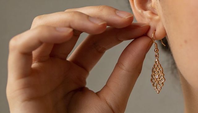 Hand adjusting gold filigree earring with sparkling stones close-up detail