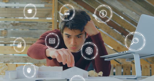 Young architect focusing on a miniature model while surrounded by digital icons. Ideal for depicting creativity, innovation in architecture, design planning, or the integration of technology in modern careers.