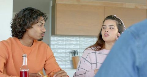 Diverse friends chatting at kitchen island sharing snack and drink during casual gathering