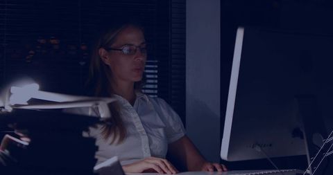 Woman Working Late in Home Office Typing on Keyboard under Desk Lamp and Monitor Light