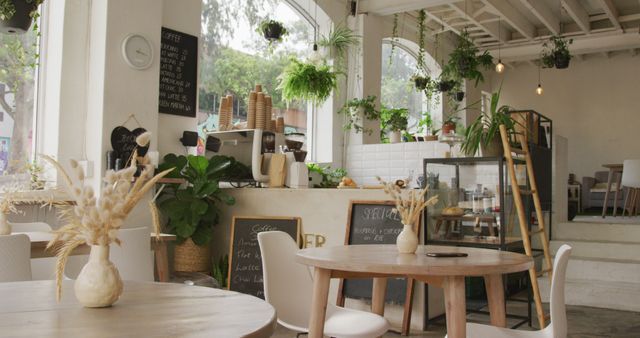 This inviting cozy urban cafe features an abundance of indoor plants, creating a refreshing and relaxing atmosphere. The natural light floods the space, highlighting the modern decor with wooden furniture. Ideal for use in projects focusing on contemporary design, small business promotion, or lifestyle blogs about cafes and urban living.