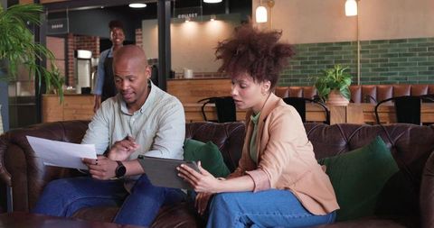 African American Professionals Collaborating on Tablet and Documents in Modern Café Workspace