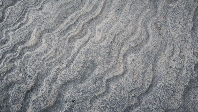 Rippled riverbed rock showcasing sinuous grooves and granular sediment texture