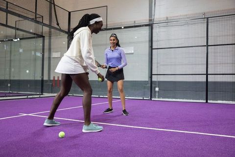 Women practicing tennis drills on purple indoor court coaching partner training teamwork