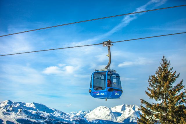 Cable car traveling over snowy alpine mountains on a clear winter day with a bright blue sky in the background. Useful for illustrating winter vacation destinations, travel and tourism in mountainous regions, ski resort activities, and adventurous outdoor experiences. Perfect for promoting winter sports and scenic landscape photography.