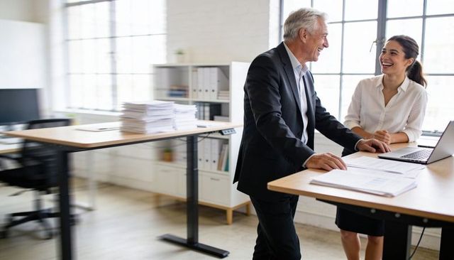 Senior manager and junior colleague collaborating at standing desk in bright modern office
