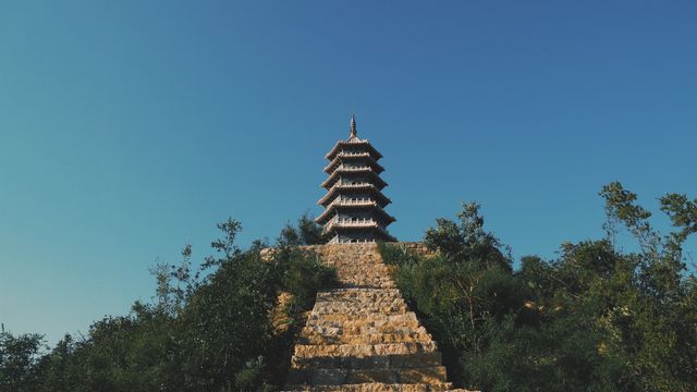 Ancient multi-tiered pagoda on top of a hill with stone steps leading up, against clear blue sky. Ideal for travel promotions, cultural heritage content, and educational materials on Asian architecture.