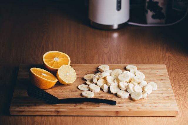 Freshly sliced bananas and oranges displayed on a wooden cutting board in a kitchen setting. Ideal for use in articles or blogs about healthy eating, organic produce, or simple food preparations. Perfect for promoting nutritious diets, recipes, or kitchen merchandise. Suitable for illustrating morning preparations and vitamins intake.