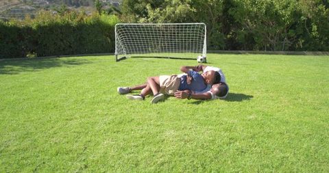 African american father and son lying on lawn near soccer goal outdoor bonding moment
