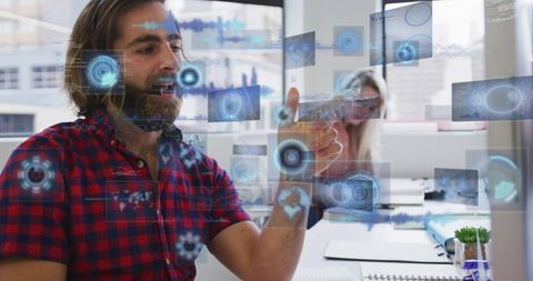Bearded man pointing at holographic interface while speaking into headset in modern office