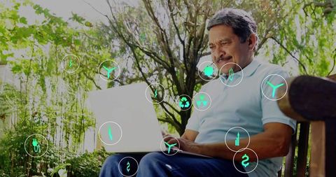Senior man using laptop in garden with floating green energy icons and data overlays