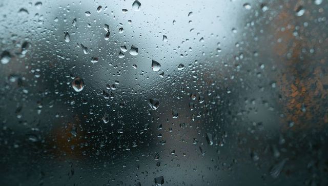 Rain-drenched car window capturing clinging water droplets and warm orange bokeh