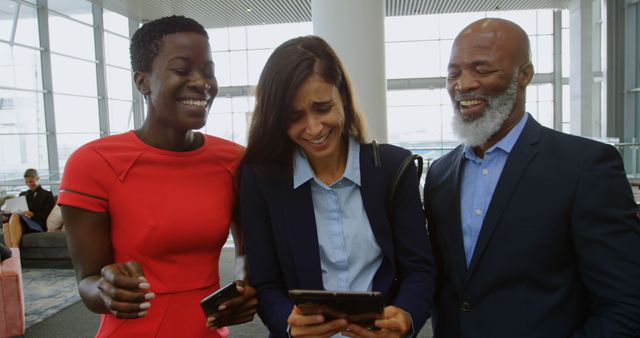 Three business colleagues, standing in modern office interior. Middle-aged man with grey beard and suit, young woman in red dress, and young woman in suit jacket, smiling and laughing while looking at a smartphone. Useful for depicting teamwork, diversity in the workplace, or professional success in advertising and corporate materials.
