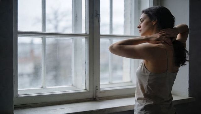Contemplative woman standing by vintage sash window looking out in minimalist studio light