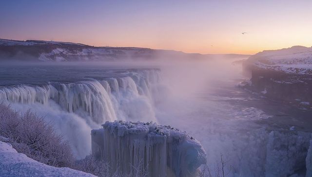 Frozen waterfall sunrise cascading mist over snowy gorge with icicle-coated rock panorama