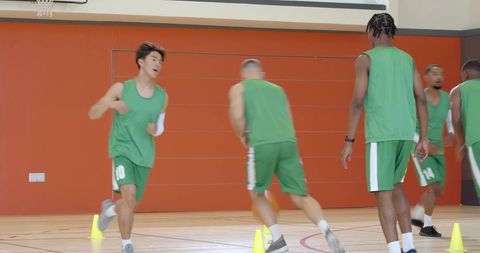 Diverse male basketball team practicing crossover dribbling through cones in indoor gym
