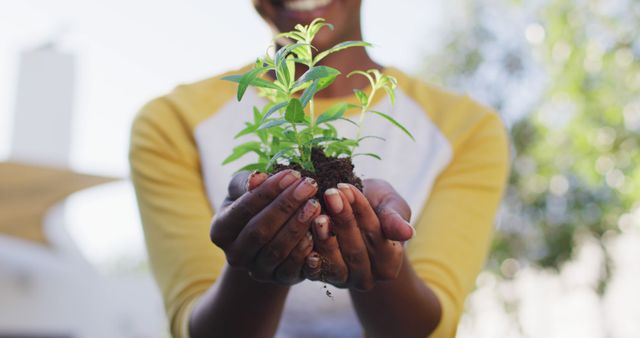 A woman holding a young plant in her hands, set against an outdoor background. This image conveys themes of nature, growth, sustainability, and gardening, making it ideal for use in environmental awareness campaigns, gardening promotions, educational materials on ecology, and social media posts focused on preserving the environment.