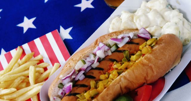 A classic American meal featuring a hot dog with condiments, French fries, and potato salad is presented on a plate with a United States flag as the backdrop. It evokes a sense of American culture and cuisine, often associated with holidays like the Fourth of July or summer barbecues.