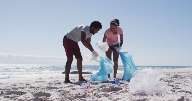 Diverse couple picking up plastic waste on a sunny sandy beach, highlighting community efforts in environmental conservation. Ideal for themes around ocean cleanup, volunteer work, eco-friendly practices, and community involvement. Useful for articles, presentations, and campaigns promoting environmental awareness and responsibility.