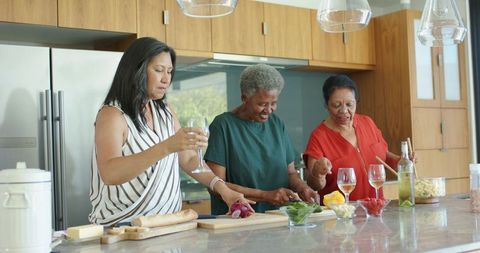 Three women cooking together in modern kitchen enjoying wine fresh ingredients
