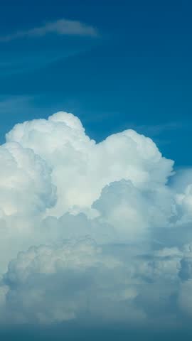 Vertical video of billowing cumulus clouds swelling and drifting across deep blue sky