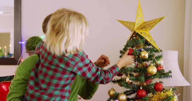 Caucasian boy decorates a Christmas tree at home. He's placing ornaments with care, capturing the festive spirit of the season.