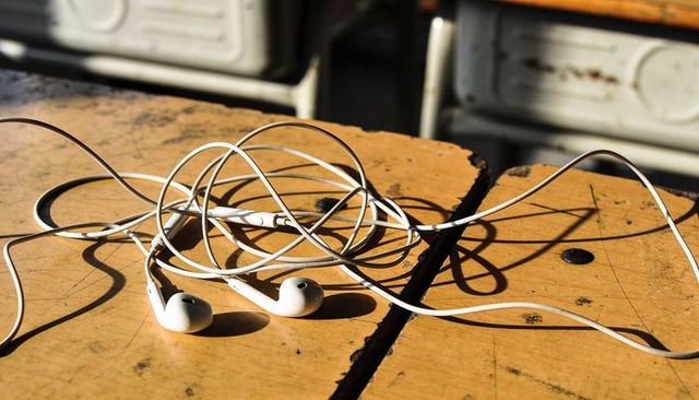 Resting tangled white earbuds on worn wooden bench casting dramatic cord shadows