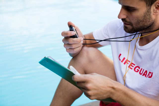 Lifeguard sitting by the pool, holding a clipboard and stopwatch, ensuring safety and monitoring swimmers. Ideal for use in articles or advertisements related to pool safety, lifeguard training, summer activities, and water safety awareness.