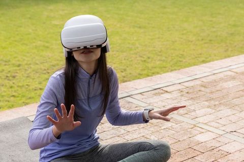 Asian woman wearing vr headset practicing outdoor fitness with smartwatch and yoga mat