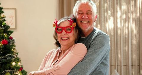 Senior Couple Embracing by Christmas Tree with Reindeer Glasses