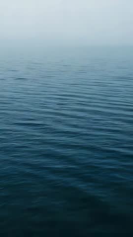 Vertical video rippling ocean surface meeting hazy horizon, tranquil blue minimalist loop