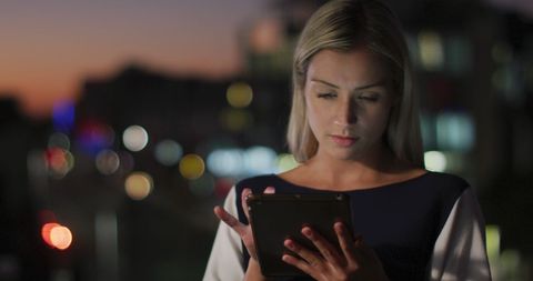 Caucasian businesswoman using tablet at night in office environment
