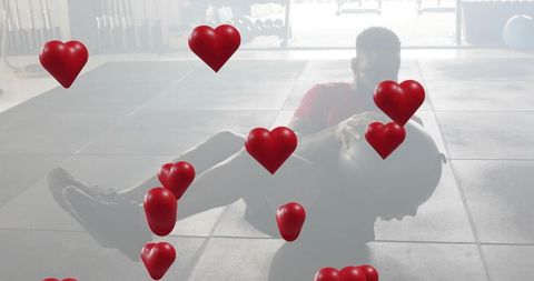 Athlete performing medicine ball core exercise on rubber tiles with floating heart overlays
