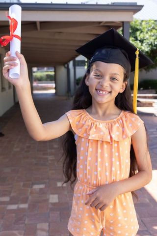 Girl wearing graduation cap holding diploma, smiling and celebrating school milestone