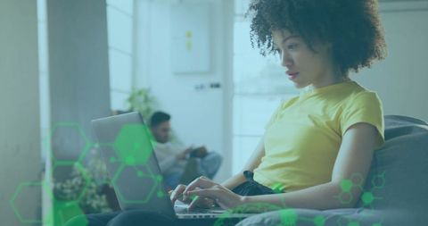 Focused Woman Typing on Laptop with Tech Overlay in Cozy Living Space