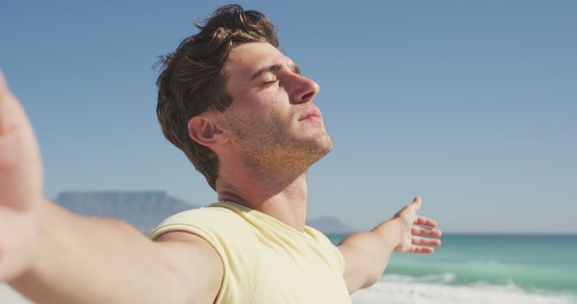 Young man with arms outstretched enjoying the fresh coastal breeze by the ocean. Perfect for themes of relaxation, freedom, mental health, wellness, outdoor activities, and nature. Ideal for marketing campaigns related to travel, leisure, and lifestyle blogs.