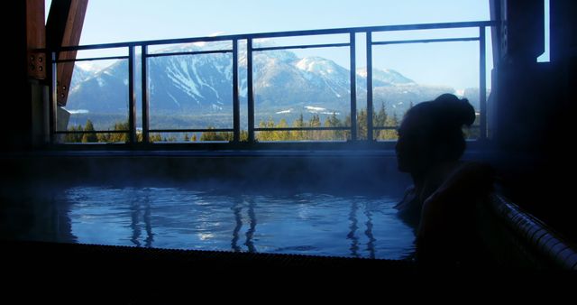 Person relaxing in steamy hot spring outdoors with snow-capped mountains in the background, perfect for websites or magazines focusing on travel, wellness, and nature retreats. Use this in content promoting relaxation, outdoor activities, and spa destinations.