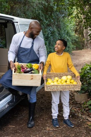 African american father and son carrying fresh farm harvest and smiling by cargo van