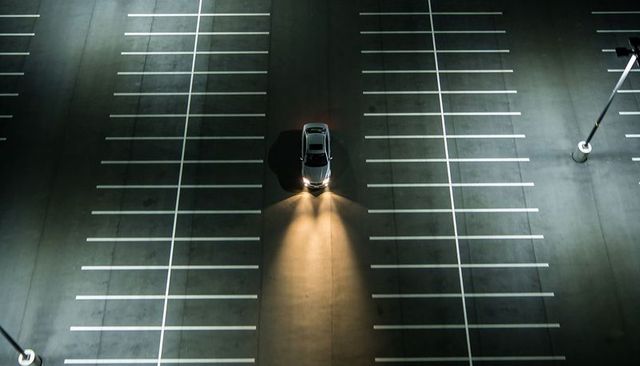 Lonely sedan illuminating empty parking lot at night from aerial view