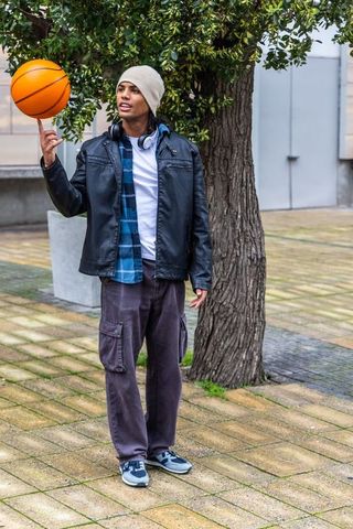 Urban youth spinning basketball on fingertip wearing headphones and casual streetwear