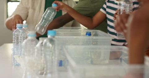 Community volunteers sorting plastic bottles for recycling on sunlit classroom table teamwork