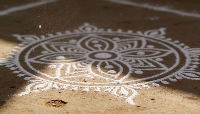 White rangoli mandala on earthen courtyard with floating powder particles and sunlight
