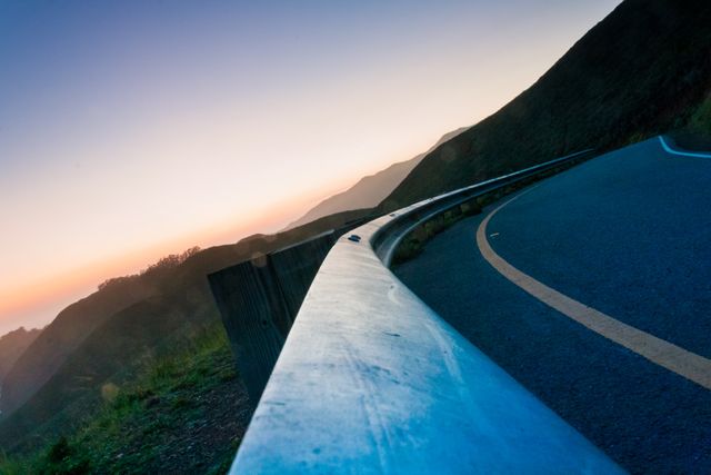 Capturing the serene beauty of a curving highway flanking mountainous terrain at sunset, this stock image is ideal for travel blogs, scenic route guides, and promotional materials for outdoor adventure activities, inviting viewers to imagine new journeys.