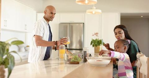 Modern family pouring orange juice and sharing breakfast at bright marble kitchen island