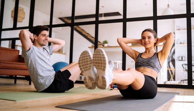 Couple holding v-sit during home core workout in sunlit modern minimalist living room
