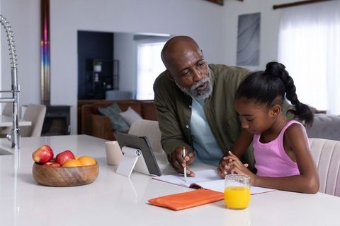 Senior african american grandfather helping granddaughter with homework at kitchen counter